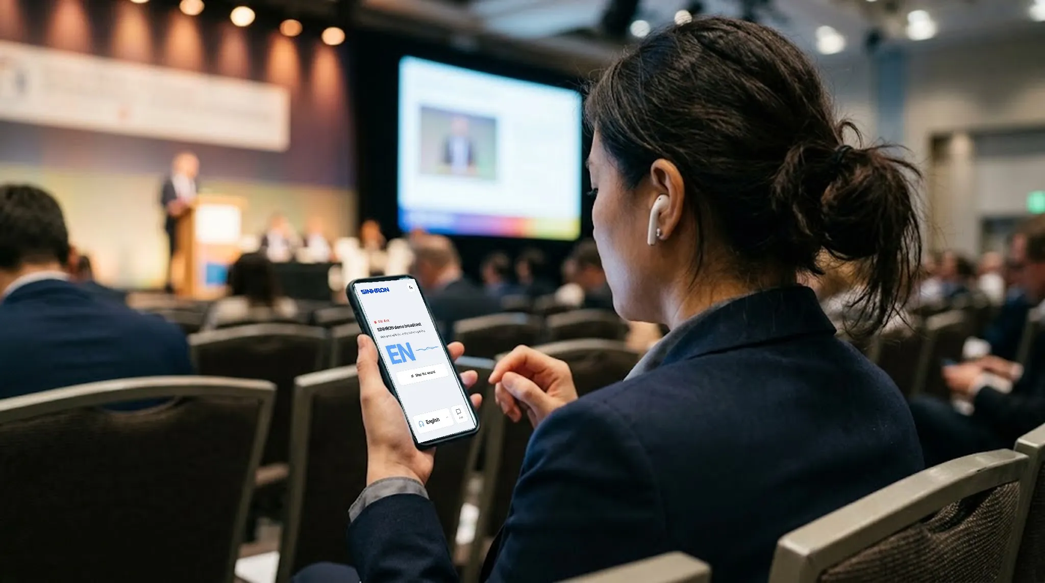 A delegate in a conference hall listens to the interpretation on her phone